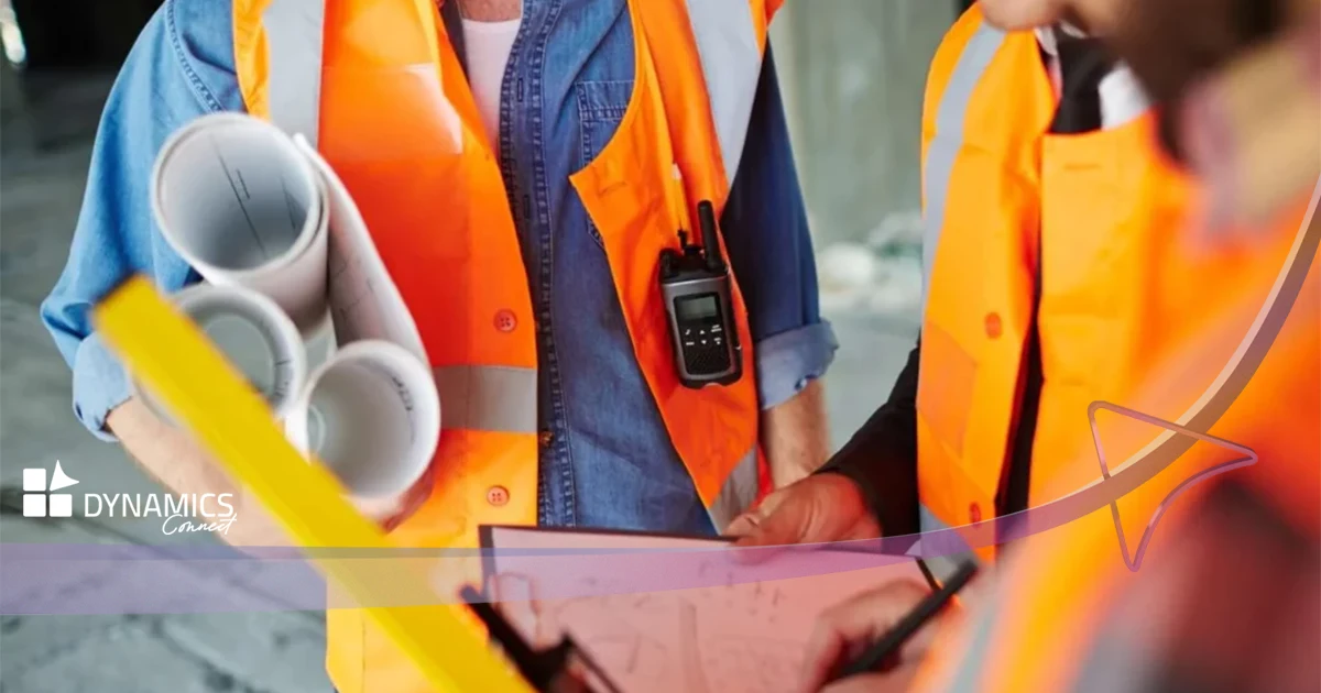 Techniciens portant des gilets de sécurité orange, discutant sur un chantier avec des plans et des équipements de communication en main.