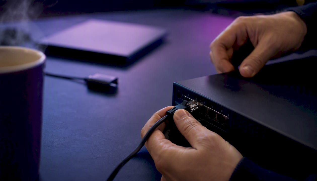 Des mains branchent un câble réseau sur un switch.