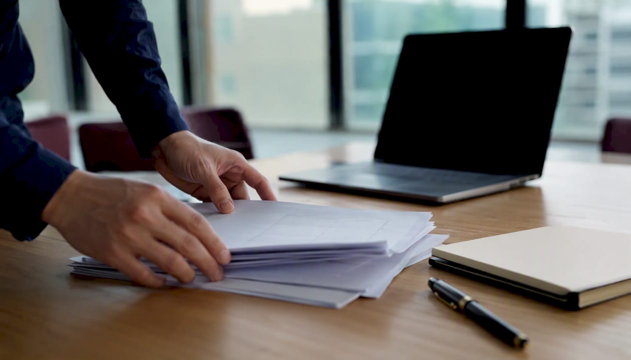 Des mains classent des dossiers d’audit CRM sur un bureau.